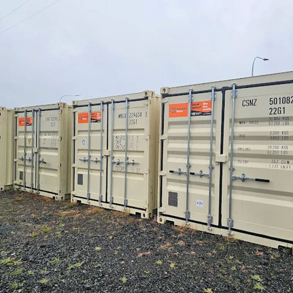 Row of tan shipping containers parked on gravel