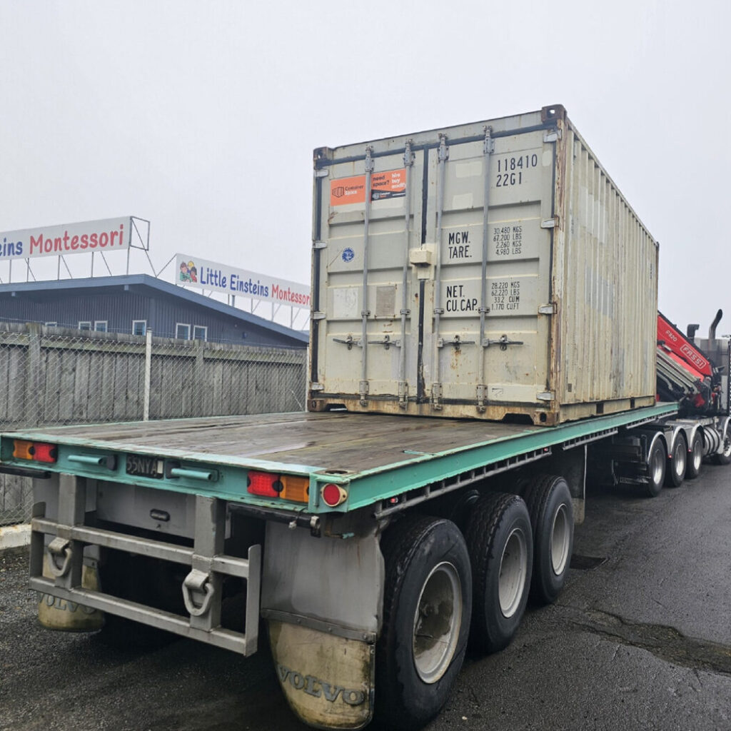 Used shipping container being delivered on a flatbed truck